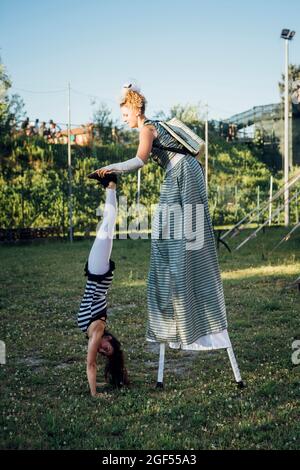 Künstlerin hilft akrobatin beim Handstand auf der Wiese Stockfoto