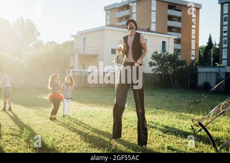 Männlicher Künstler jongliert mit Bällen, während er mit Stelzen auf Gras steht Stockfoto