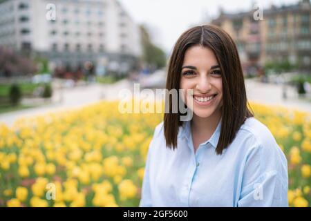 Lächelnd schöne junge Frau vor gelb blühenden Pflanzen Stockfoto