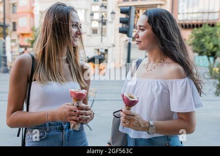 Junge Frauen halten Eiszapfen, während sie sich in der Stadt angucken Stockfoto