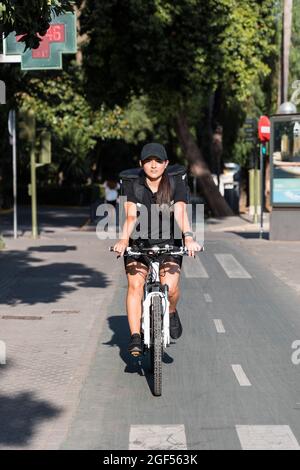 Junge, wichtige Servicearbeiterin, die an sonnigen Tagen Fahrrad auf der Straße fährt Stockfoto