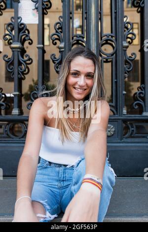 Junge, schöne blonde Frau, die vor dem Metalltor sitzt Stockfoto