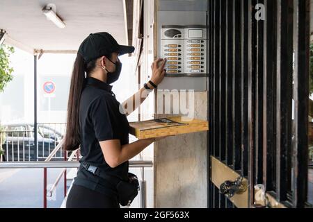 Junge Pizzaliefererin hält Box, während sie während einer Pandemie an der Türklingel klingelt Stockfoto