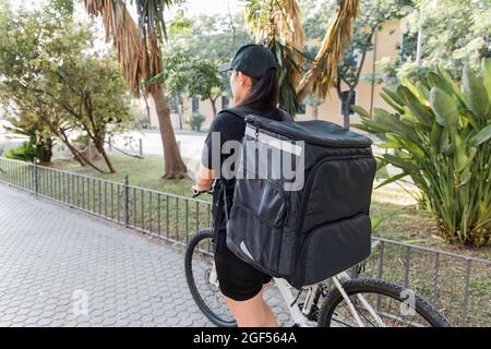 Weibliche Entbindung Person trägt Rucksack, während Fahrrad auf dem Fußweg Rollen Stockfoto