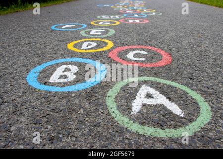 Buchstaben des Alphabets in farbigen Kreisen auf einer asphaltierten Straße Stockfoto