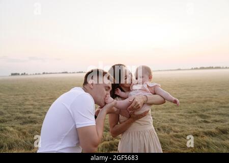 Vater küsst die Füße der Tochter, während die Mutter sie auf dem Feld trägt Stockfoto