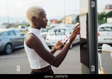 Frau, die ein Touchscreen-Gerät an der Stange am Fahrradparkplatz verwendet Stockfoto