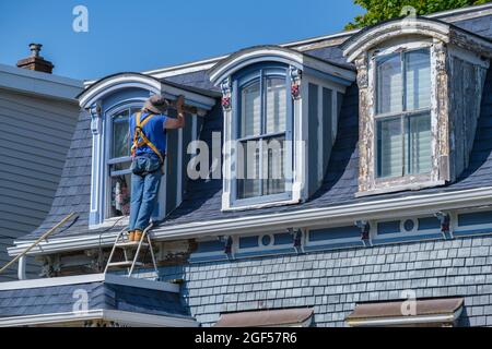 Dartmouth, Kanada - 10. August 2021: Arbeiter schleift Farbe an die Wand eines alten Hauses. Stockfoto