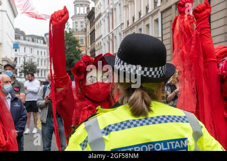 London, Großbritannien. August 2021. Ein Mitglied der Roten Rebellion-Brigade des Extinction Rebellion hebt ihren Arm mit geballter Faust, als sie sich während des Tages des Extinction Rebellion, einer zweiwöchigen Demonstration in Zentral-London, mit einem Polizisten konfrontiert sieht. Extinction Rebellion veranstaltete einen Protest gegen den Klimawandel, die globale Erwärmung, Das plant, die Ursache der Klima- und Umweltkrise zu treffen und die Regierung vor der COP26 der UN-Klimakonferenz 2021 zu fordern, die Unternehmen aus fossilen Brennstoffen zu veräußern. Kredit: SOPA Images Limited/Alamy Live Nachrichten Stockfoto