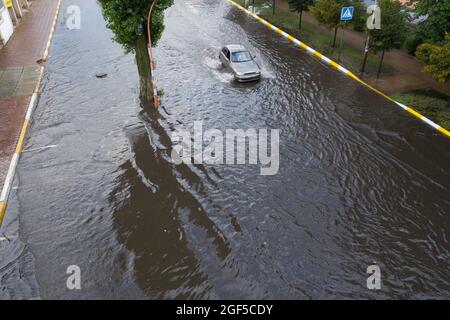 Überflutete Straße nach einem ungewöhnlichen Regenguss in den Vororten. Autos bewegen sich auf der überfluteten Straße. Folgen einer Naturkatastrophe. Stockfoto