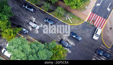 Überflutete Straße nach einem ungewöhnlichen Regenguss in den Vororten. Autos bewegen sich auf der überfluteten Straße. Folgen einer Naturkatastrophe. Stockfoto