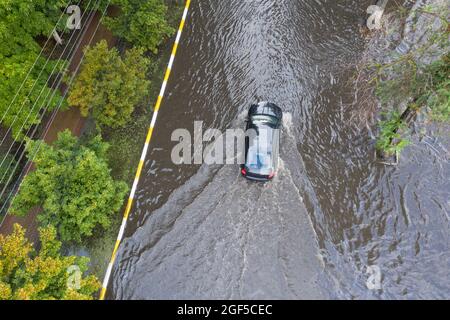 Überflutete Straße nach einem ungewöhnlichen Regenguss in den Vororten. Autos bewegen sich auf der überfluteten Straße. Folgen einer Naturkatastrophe. Stockfoto