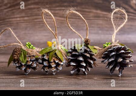 Handgemachtes Weihnachtsbaumspielzeug aus Kiefernzapfen, verziert mit natürlichen Materialien, vor dem Hintergrund eines geschnittenen Baumes. Dekorationen mit Hanf-Suspension Stockfoto