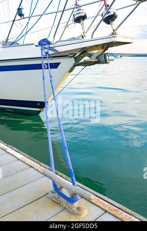 Ein Boot, das an einem Ponton festgemacht ist, befestigt über ein blaues Seil, das um einen Strang gebunden ist. Stockfoto