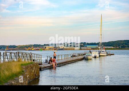 Boote vertäuten auf dem Ponton in Hazelbeach, Milford Haven in Pembrokeshire, Wales. Die Leute sitzen und entspannen sich am Rand des Pntoons und paddeln. Stockfoto