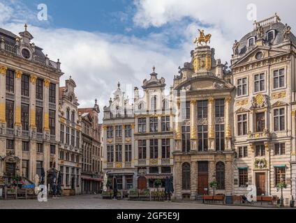 Brüssel, Belgien - 31. Juli 2021: Fassaden historischer Gildenhäuser auf der SW-Seite des Grand Place unter blauer Wolkenlandschaft. Goldene Statuen und Ornamente. Stockfoto