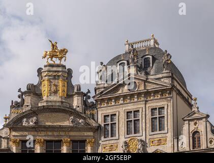 Brüssel, Belgien - 31. Juli 2021: Oben auf 2 Fassaden historischer Gildenhäuser auf der SW-Seite des Grand Place unter blauer Wolkenlandschaft. Goldene Statuen und Ornam Stockfoto