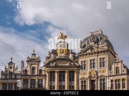 Brüssel, Belgien - 31. Juli 2021: Fassaden historischer Gildenhäuser auf der SW-Seite des Grand Place unter blauer Wolkenlandschaft. Goldene Statuen und Ornamente Stockfoto