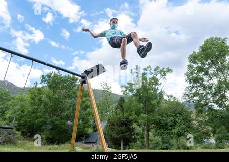 Der junge Mann mit einer Damenmaske springt von einer Schaukel auf einem Spielplatz und springt in die Leere Stockfoto