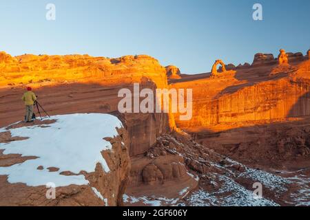 Fotograf fotografiert Delicate Arch vom Delicate Arch Viewpoint bei Sonnenaufgang mit Schnee im Winter, Arches National Park, Utah Stockfoto