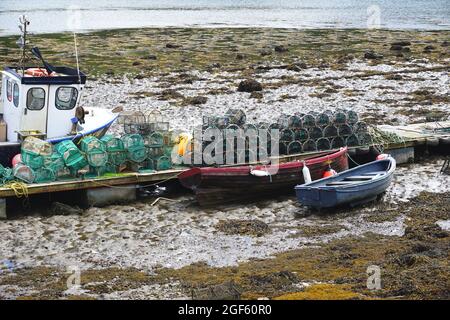 Fischerboote wurden bei Ebbe auf felsigen Gezeitenebenen neben einem Dock mit Hummer-Töpfen und Garnelenschalen im Dorf Plockton, Schottland, befahren Stockfoto