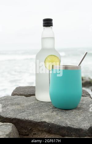 Türkisfarbener Shaker mit einer Zitrone und einer Flasche Alkohol auf einigen Felsen im Meer. Pisco Stockfoto