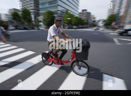 Tokio, Japan. August 2021. Ein Mann fährt mit einem roten Fahrrad durch einen Fußgängerüberweg. Kredit: Marcus Brandt/dpa/Alamy Live Nachrichten Stockfoto