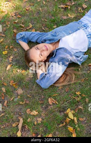 Digitales Detox-Konzept - nachdenkliche junge Frau liegt im Park auf dem Rasen. Sie macht eine Pause von der Büroarbeit. Stockfoto