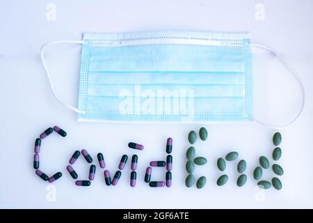 Inschrift Covid Ende von farbigen Tabletten mit medizinischer Maske Stockfoto