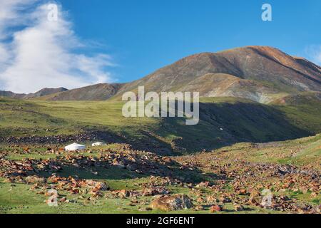 Mongolische Landschaft mit Bergsteppe unter fliessenden Kumuluswolken am blauen Himmel, Jurten und Ziegenherden. Natürliche Berggrenze Tsagduult, westlich Stockfoto