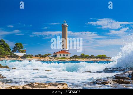 Meereswellen brechen an Land, Leuchtturm von Veli Rat auf der Insel Dugi Otok, Kroatien im Hintergrund Stockfoto