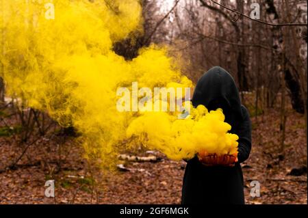 Eine gruselige Hexe hält einen dampfenden Kürbis in einen tiefen Wald. Jack o Laterne strahlt für halloween gelben Rauch aus Stockfoto