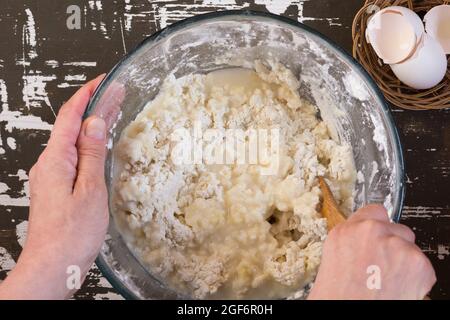 Frau Hände mischen heißes Wasser und Mehl, um Teig mit Holzlöffel auf dem braunen Hintergrund zu machen Stockfoto