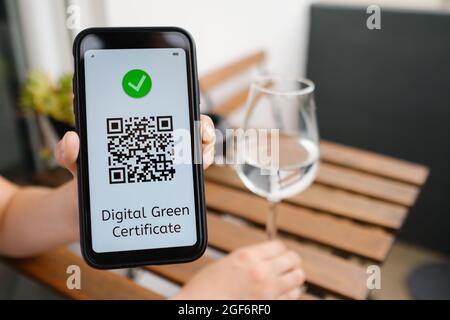 Frau demonstriert digitales grünes Zertifikat mit QR-Code im Mobiltelefon, das im Café sitzt. Stockfoto