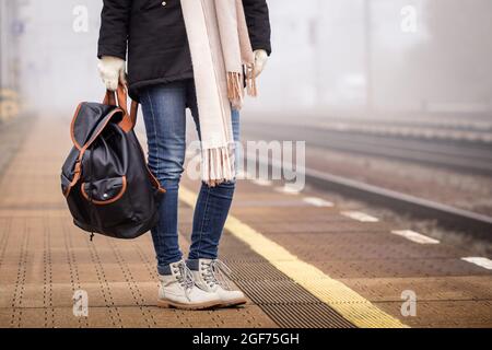 Reisender mit Rucksack, der am Bahnhof steht und auf den Zug wartet. Frau in Jeans und Stiefeln Stockfoto