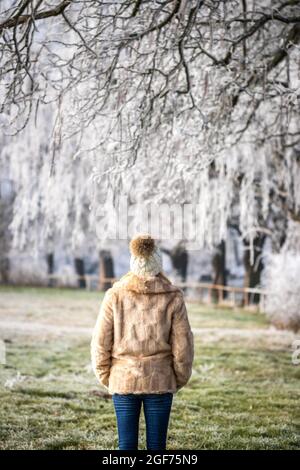 Frau in Kunstpelzmantel und genießen Spaziergang im Winter Park. Schöne verschneite Landschaft mit gefrorenen Bäumen Stockfoto
