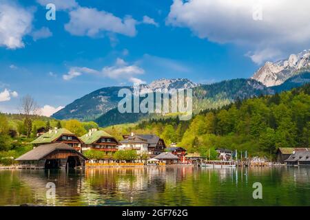 Herrlicher Panoramablick auf die Gemeinde Schönau am Königssee mit traditionellen bayerischen Häusern, Bootshäusern, einem Boot an der Seebrücke und dem... Stockfoto