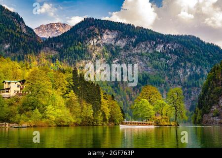 Schöne ruhige Landschaft mit Blick auf ein weißes Boot, das an der kleinen Christlieger-Insel am berühmten Königssee vorbeifährt. Im Hintergrund sind die... Stockfoto