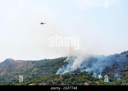 Feuern Sie einen Hubschrauber, der Wasser aus einem Eimer auf ein Waldfeuer in den Bergen ablässt. Waldbrände sind eine Umweltkatastrophe. Entwaldung. Stockfoto