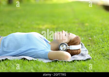 Seitenansicht Porträt einer entspannten Frau, die Musik hört, mit Kopfhörern, die auf dem Gras in einem Park liegen Stockfoto