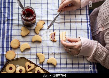 Vorbereitung von gebackenen Weihnachts Linzer Süßigkeiten. Frau füllt hausgemachte Kekse mit roter Johannisbeermarmelade Stockfoto