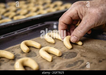 Ältere Frau setzt Vanille-Halbmondbrötchen weiß als Vanillekipferl auf Backblech hausgemachte weihnachtsbonbons bereit zum Backen Stockfoto