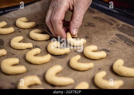 Alte weibliche Hände, die kleine Vanillehalbmondkekse mit Backblech auf das Blech legen. Machen Tradition weihnachtsplätzchen Stockfoto