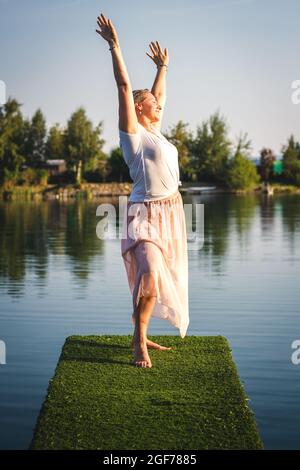 Plus size Frau mit erhobenen Armen trainieren im Freien am See. Glückliche übergewichtige Frau, die im Sommer Sonnenlicht genießt. Gesunder Lebensstil Stockfoto
