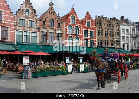 Pferdekutsche mit Touristen und Gildenhäuser mit Restaurants auf dem Marktplatz von Brügge, Provinz Westflandern, Belgien Stockfoto