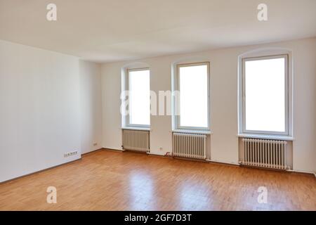 Leeres großes weißes Zimmer in der Wohnung mit Heizkörpern unter den Fenstern im alten Gebäude Stockfoto