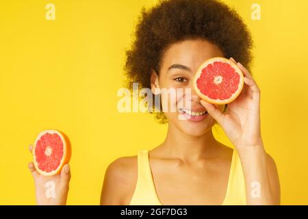 Fröhliche Afro-Frau hält rot-orange Scheiben Stockfoto