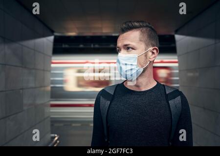 Mann mit Gesichtsmaske in U-Bahn-Station. Porträtieren Sie den Passagier in unscharfen Bewegungen gegen den Zug. Stockfoto