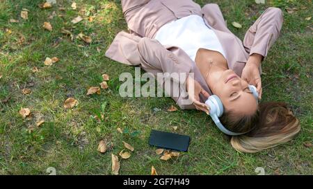 Draufsicht auf eine Frau, die die Musik genießt, während sie im Stadtpark auf dem Rasen laugt. Sie erholte sich von der Büroarbeit. Stockfoto