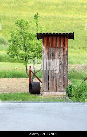 Kleiner, kleiner, selbstgemachter Gartenwerkzeugschuppen aus vertikalen Holzbrettern und mit Vorhängeschloss am Rand des gepflasterten Vorstadtfamilienhauses im Hinterhof gesichert Stockfoto